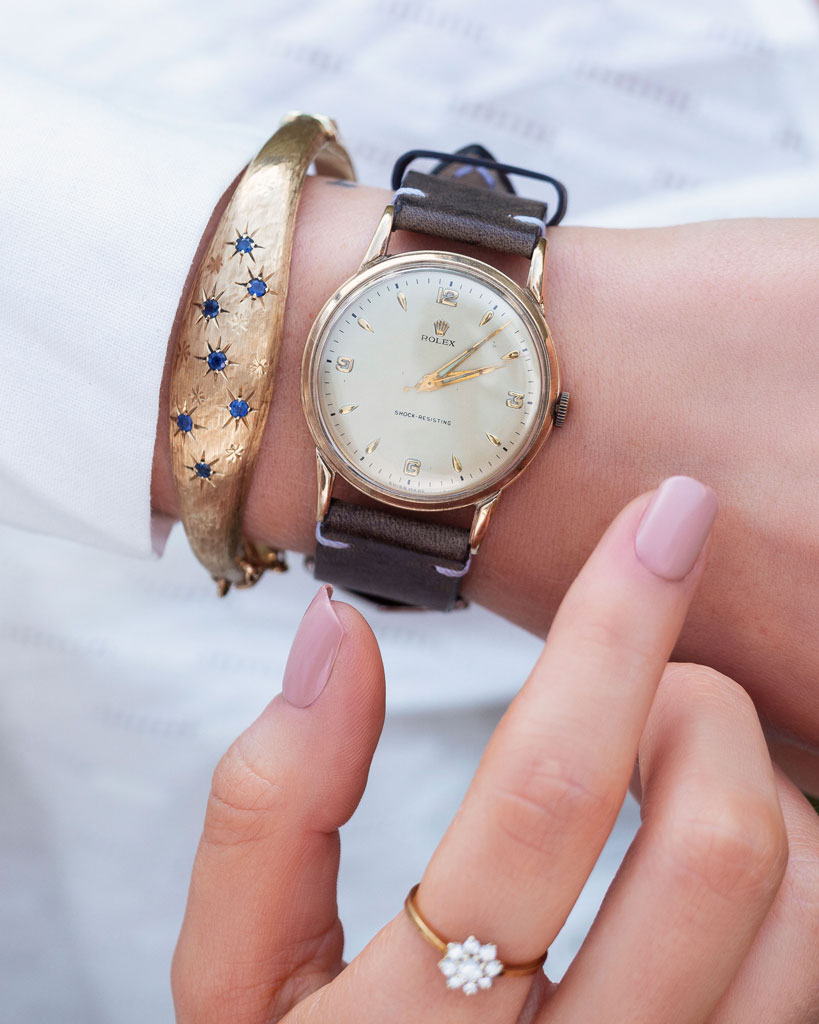 Close-up of a person's wrist wearing a pre-owned vintage Rolex watch with a brown strap, alongside a gold bracelet.